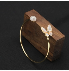 Detail of gold butterfly bracelet with white pearl and zircon on rustic wood base