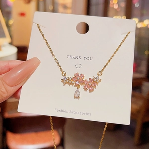 Close-up of golden necklace with pink crystal flowers and a water drop pendant