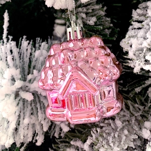 Pink house-shaped Christmas tree ornament with metallic finish hanging on snowy branch