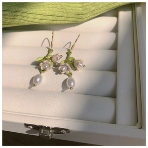 Detail of lily of the valley earrings with green leaves and pearls on beige velvet