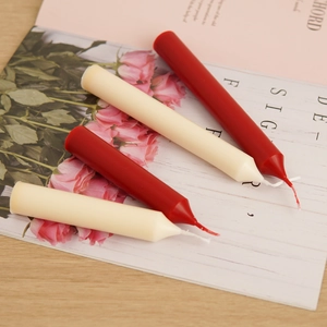 Flat lay of slim taper candles in red and beige with cotton wicks on floral paper background