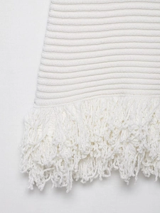 Detail of cream white knit texture and elegant long fringe tassels on the dress hem
