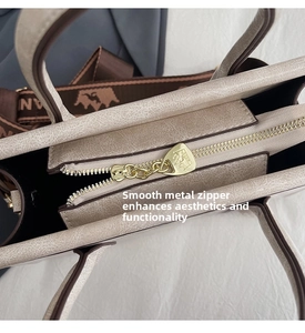 Close-up of smooth gold-tone zipper hardware and logo puller on a textured tote bag