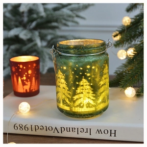 Detail of green glass Christmas candle holder with festive tree patterns and LED light