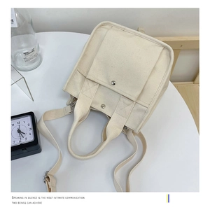 Detail of off-white canvas tote bag with metal buckle pocket and dual shoulder straps