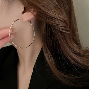 Close-up of a large gold textured hoop earring worn by a model for a stylish look