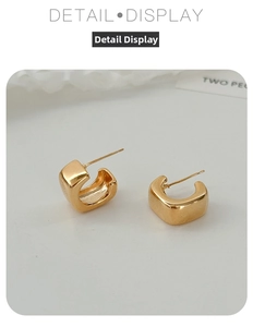 Close-up of square C-shaped gold metal earrings on a minimalist white background