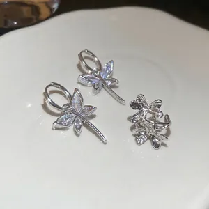 Silver flower and butterfly drop earrings set with zircon stones on white ceramic tray
