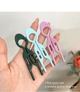 Three U-shaped minimalist hair pins in green blue and pink held by hand for bun styling