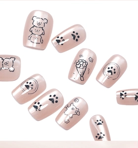 Macro detail of pearl pink press-on nails with black hand-drawn cartoon puppy and floral patterns