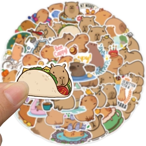 Hand holding a cute capybara taco sticker with various waterproof cartoon decals in the background