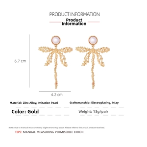 Detailed view of gold alloy dragonfly earrings with ribbon bow and faux pearl accents
