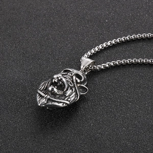 Detailed view of silver lion head and skull pendant on a stainless steel box chain