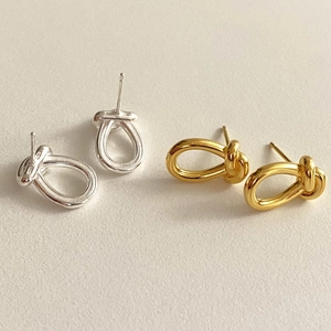 Detailed view of polished gold and silver knot stud earrings on a beige textured backdrop