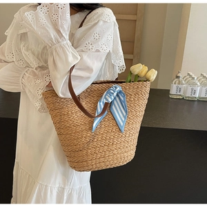Straw woven tote bag with blue striped scarf and brown leather strap on model shoulder