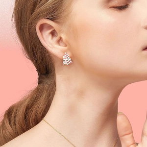Close-up of elegant Christmas tree stud earrings with white enamel and colorful details
