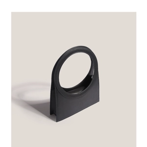 Minimalist black trapezoid leather handbag with round handle on a neutral background