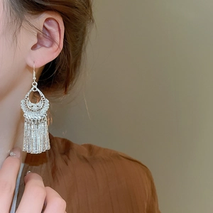 Close-up of silver geometric tassel earrings worn by model showing long drop fringe detail