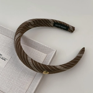 Détail d'un serre-tête rayé marron foncé avec cœur doré et étiquette Hand Made