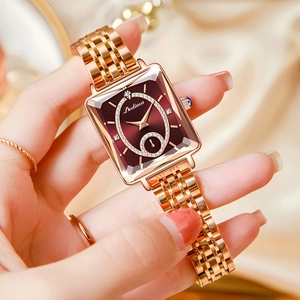Close-up of rose gold square watch with burgundy dial and crystal markers on wrist