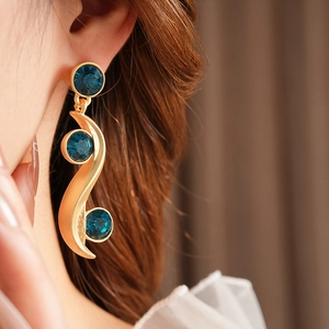 Detailed view of matte gold S-shape earring with three round blue gemstones on ear