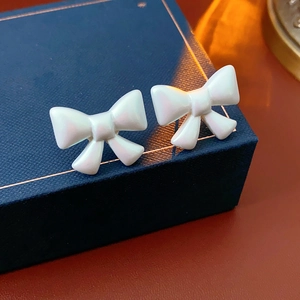 Close-up of white pearlescent bow earrings on a blue jewelry box with warm lighting