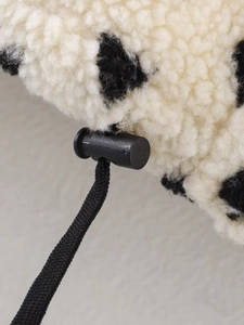 Detail of black plastic drawstring toggle on black and white polka dot fleece jacket