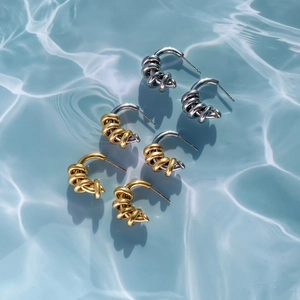 Detailed view of three twisted knot C-shaped earrings in gold and silver over blue ripples