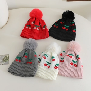 Detailed flat lay of children's knit beanies in five colors with cherry pattern and pom-poms