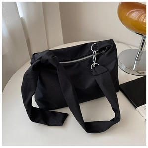 Close-up of black canvas crossbody bag with silver chain detail on a white table