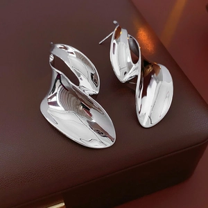 Macro shot of silver irregular twisted leaf earrings on dark brown leather background