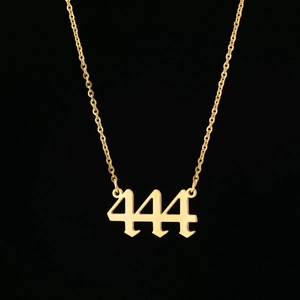 Gros plan du pendentif doré chiffre ange 444 avec chaîne fine sur fond noir élégant