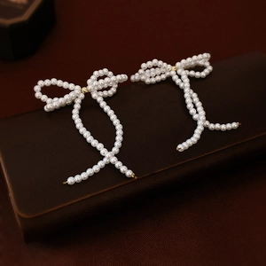 Macro shot of elegant white faux pearl bow earrings with intricate beaded craftsmanship
