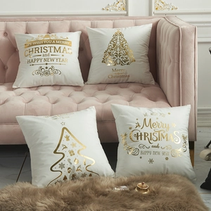 Set of four white Christmas pillow covers with gold holiday patterns on a pink sofa