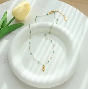 Detailed shot of a gold tulip pendant necklace with green crystal beads on a white ceramic plate