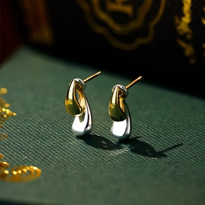 Minimalist two-tone teardrop earrings in gold and silver finish on a green display
