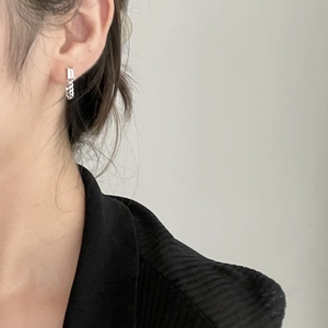 Detailed close-up of a silver chain drop earring with a rectangular zircon stone on ear