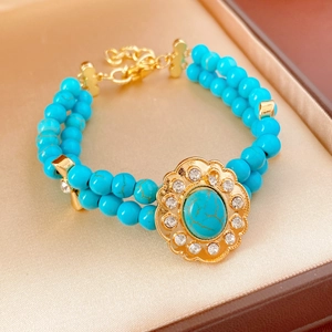 Gros plan d'un bracelet double couche avec perles turquoise et fleur dorée dans un écrin à bijoux