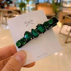 Close-up of a green crystal bow hair clip with black fabric base and metal spring