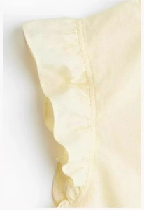 Detailed close-up of light yellow linen blend fabric with ruffle cuff and stitching texture