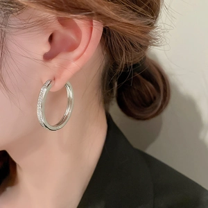 Close-up of large silver hoop earrings with micro-inlaid diamonds on a female model