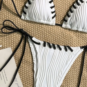 Macro shot of white ribbed bikini fabric featuring silver eyelets and black lace-up strings