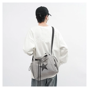 Gray nylon messenger bag with black star patch shown on a model's back in a bright studio