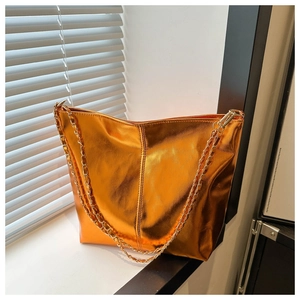 Detail of glossy orange bucket bag with gold chain strap placed by a window