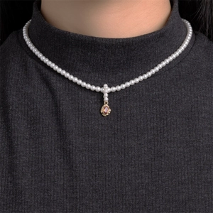 Detail of pearl cross necklace featuring a gold oval pendant with orange gemstone