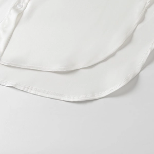 Détail de la chemise élégante en satin blanc montrant l'ourlet arrondi et les coutures
