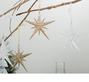Close-up of sparkling champagne gold and white star ornaments hanging on a rustic branch