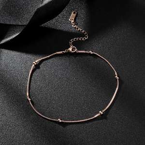 Detail of rose gold titanium bead anklet with lobster clasp on textured surface