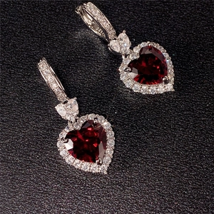 Detalle de pendientes de corazón plateados con gema roja oscura y halo brillante
