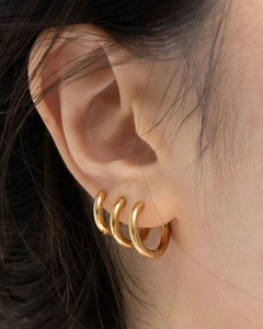 Macro close-up of golden tubular hoop earrings worn on ear lobe and cartilage